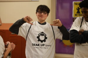 A middle school boy points to the GEAR UP Iowa logo on a shirt he's wearing