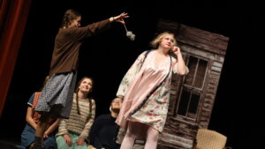 A high school student dressed as an orphan holds up a fake rat in front of another student dressed as Miss Hanagan's character during "Annie the Musical."