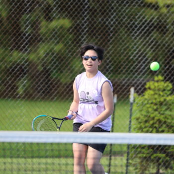 A member of the BHS JV girls tennis team goes to whack a tennis ball with her racket.