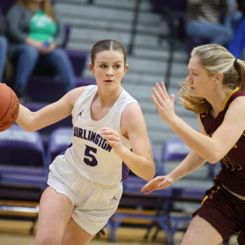 A member of the girls basketball team dribbles the ball past a member of the opposing team.