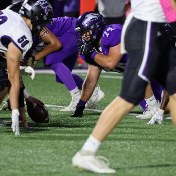 A football player stares down an opposing player while crouched down on the field.