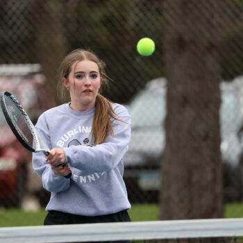 A member of the girls tennis team readies herself to hit the tennis ball flying toward her with her racket.