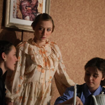 A teen girl looks at her two seated cast members during dress rehearsal for the spring play 