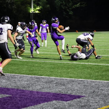 A football player spin jumps over a member of the opposing team en route to a touchdown.