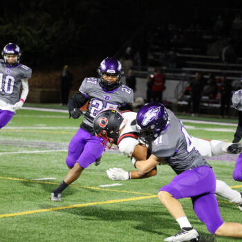 A football player tackles a member of the opposing team while his teammates run toward them.