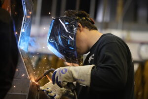 Sparks fly as a student wearing a welding mask welds.