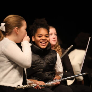 A girl smiles while holding a flute in her lap at the start of a music concert at Aldo Leopold Intermediate School.