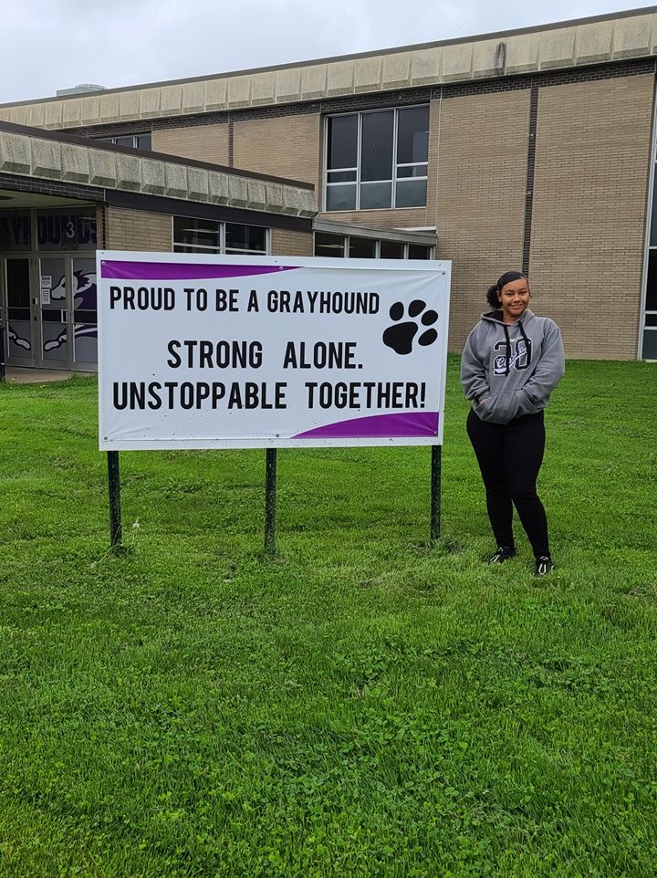 Riana Bratton stands outside Burlington High School that says "Proud to be a Grayhound
Strong Alone.
Unstoppable Together!"