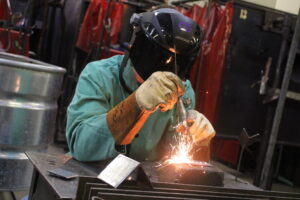 Sparks fly as a student welds a piece of metal.