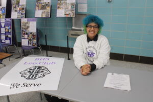 A student sits at a table with a Leo Club poster on top of it during an informational night for incoming ninth-graders.