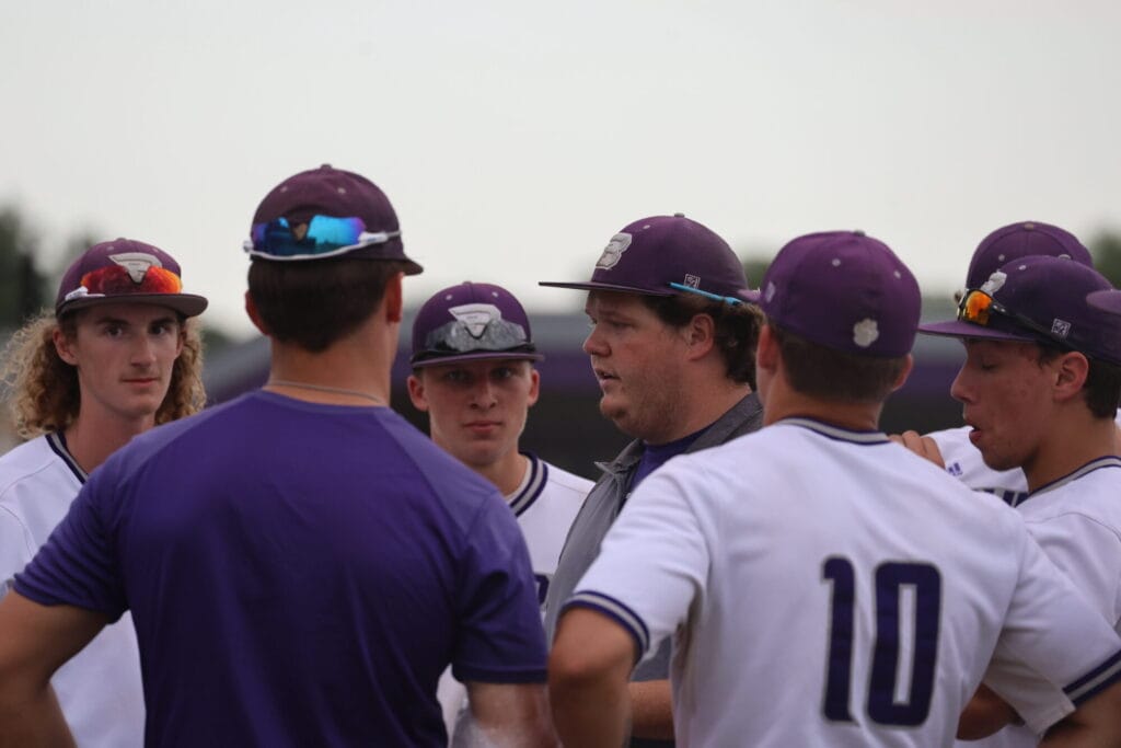 Baseball players surround their coach during a game.