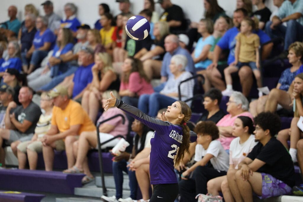 A volleyball player serves the ball during a game while the crowd watches from the bleachers in the background of the BHS gymnasium.