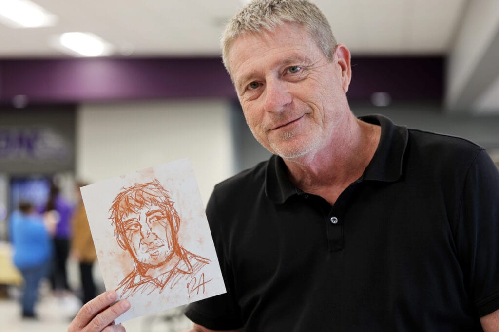 Brian Blake, a science teacher at Burlington High School, holds up a sketch drawn of him by Paulina Aguilera Tuesday, April 22, 2025, as part of a student demonstration in the school cafeteria.