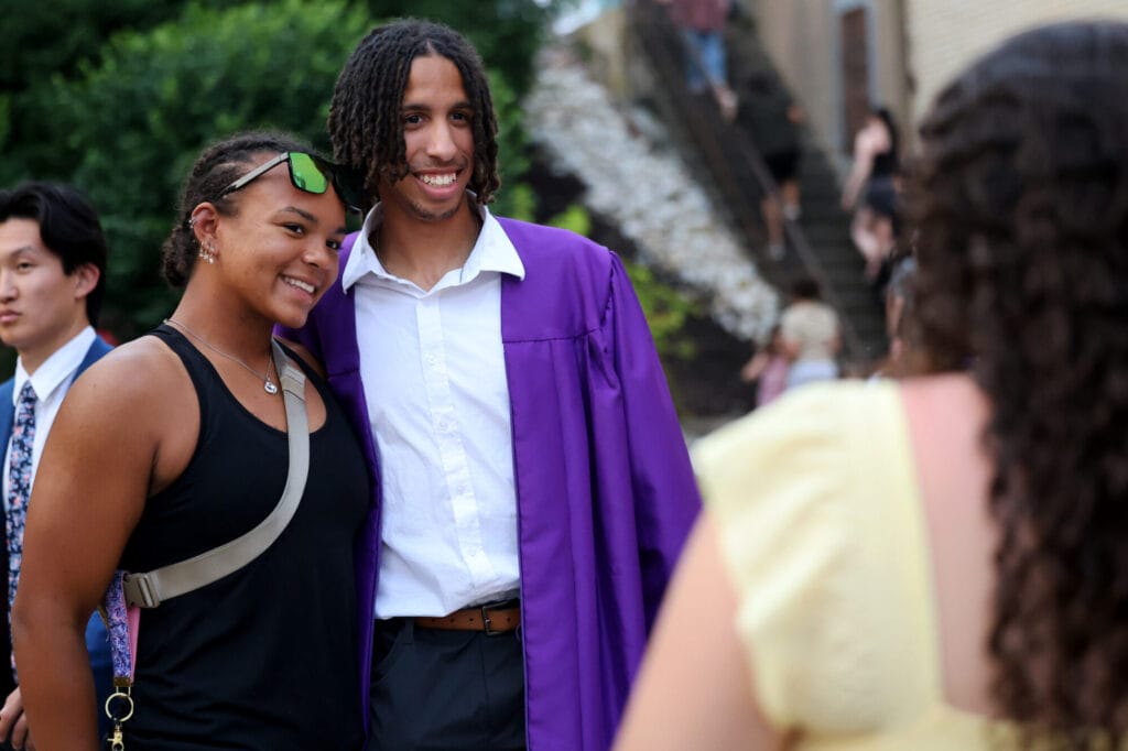 A graduate and friend smile and stand shoulder-to-shoulder while posing for a photo following Burlington High School's 2025 commencement ceremony at Bracewell Stadium.