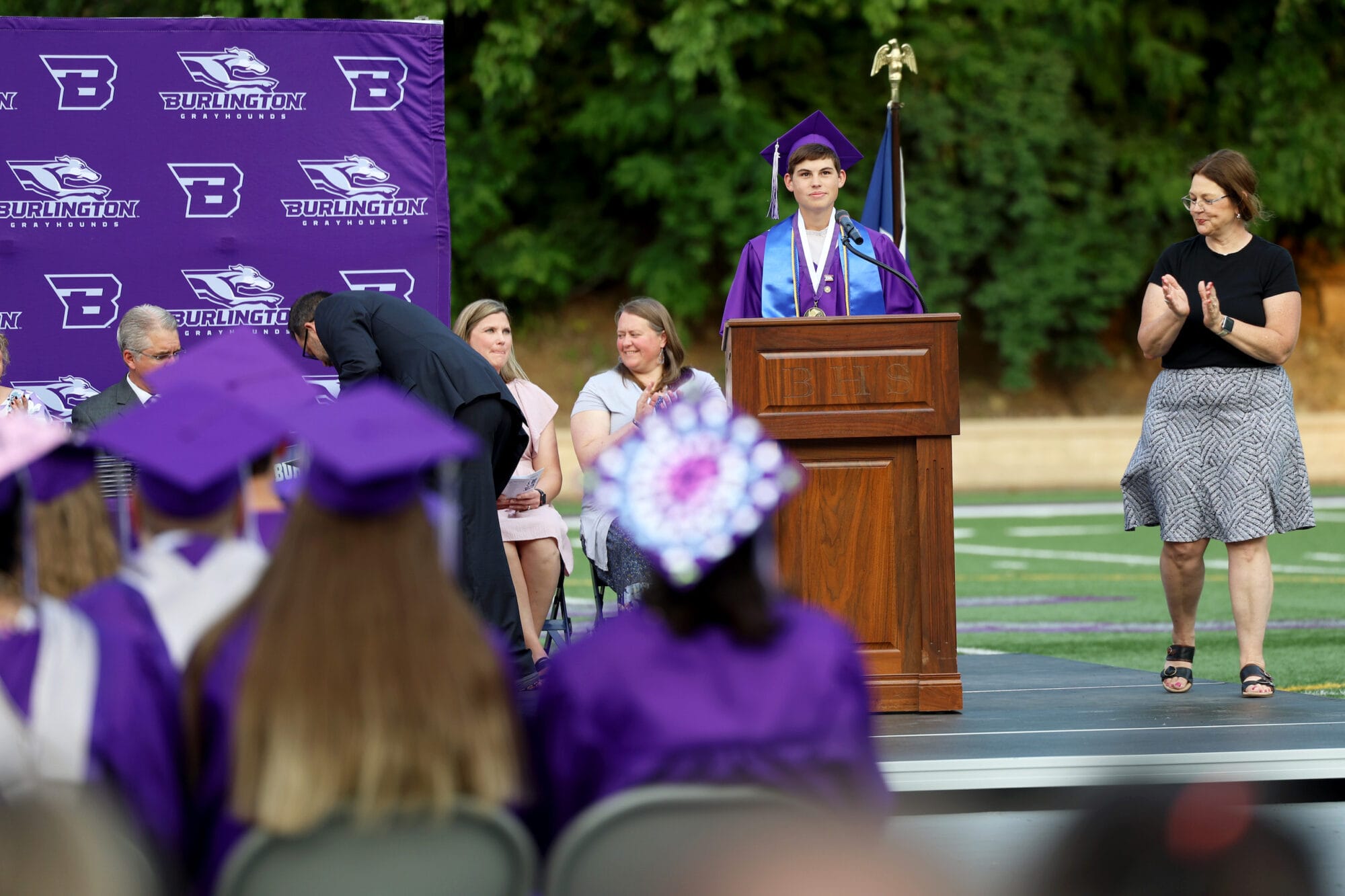 Salutatorian Peyton Strabala looks out at the crowd while standing behind a podium before delivering his speech during Burlington High School's 2025 commencement ceremony at Bracewell Stadium.