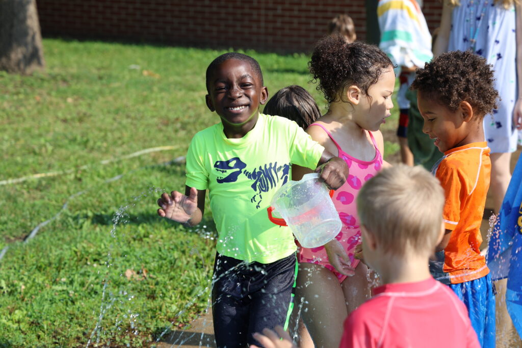 A group of children play outside in a sprinkler during water play day in Corse Early Childhood Center's child care program.