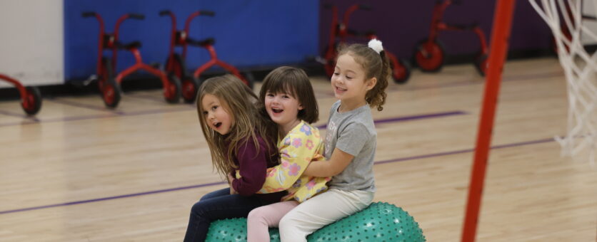 Three girls laugh while sitting on a large ball