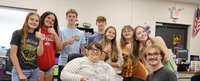 A group of students and their teacher pose for a photo in their Spanish classroom.