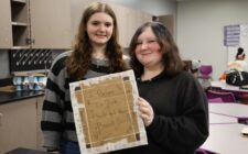 Freshmen Kassidy Korte and Maddie Moore hold up the chest plate they designed Jan. 16, 2025, in Brian Blake’s Physical Science class before testing its ability to reduce force. In addition to protective layers of tape, plastic bags, cups, cardboard, and cotton balls, they added an uplifting message to their design.