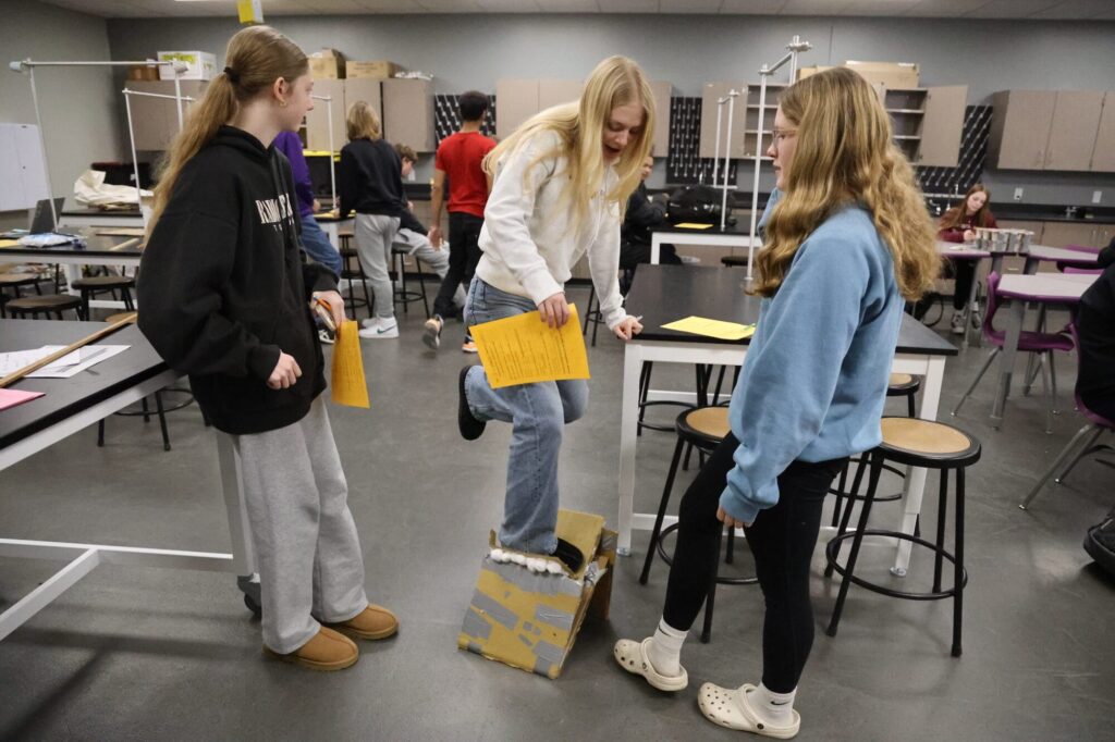 Freshman Florrah Mehaffy gives her chest plate one final test while co-builders Josie Newell and Saoirse Hermann look on Jan. 16, 2025, in Brian Blake’s classroom at Burlington High School. Despite having tested the most effective of the chest plates in their class, the structure could not hold up to the power of a teen-sized human.