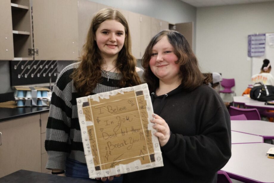 Freshmen Kassidy Korte and Maddie Moore hold up the chest plate they designed Jan. 16, 2025, in Brian Blake’s Physical Science class before testing its ability to reduce force. In addition to protective layers of tape, plastic bags, cups, cardboard, and cotton balls, they added an uplifting message to their design.