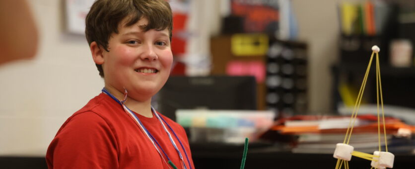 A boy smiles while putting beads on pipecleaner