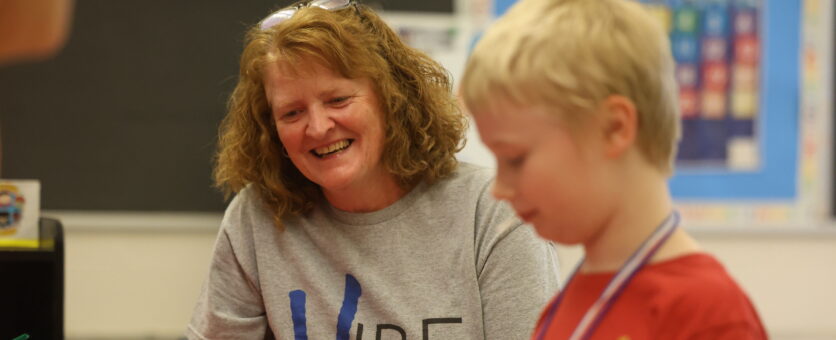 A teacher smiles while her student puts together a craft