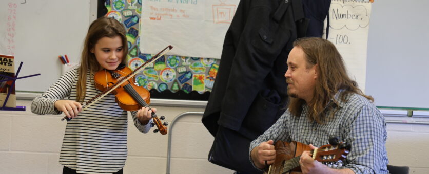 A girl plays the violin while her teacher plays the guitar