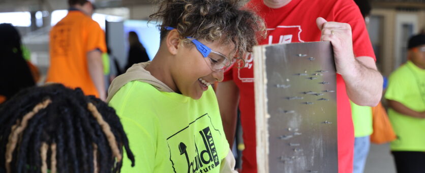 A middle school boy smiles while using a power screwdriver during an outdoor career expo