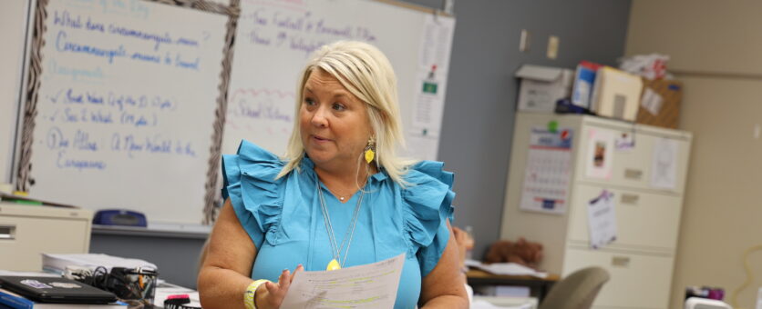 A teacher stands in front of her classroom holding a piece of paper