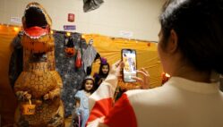 A parent takes a photo of her daughters next to an inflatable dinosaur Oct. 29, 2024, at Edward Stone Middle School during the Haunted Halls event.