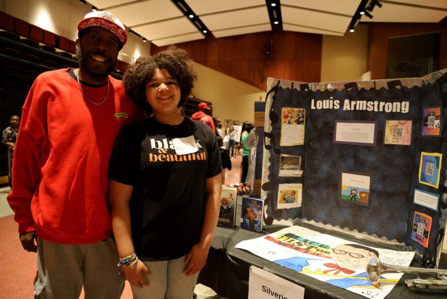 Demond Carr and his daughter, fifth-grader Journey Carr, pose for a photo alongside an exhibit about Louis Armstrong Thursday, Feb. 17, 2025, during Aldo Leopold Intermediate School’s fourth annual Black History Museum. The exhibit was one of more than 20 student-led projects on display.