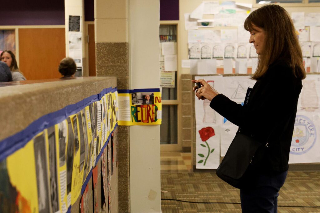Susan Stone takes pictures of a timeline of her father’s life prepared by Edward Stone Middle School students Monday, April 28, 2025, in the first floor commons area of the middle school. She was among nearly 20 of the late Dr. Edward Stone’s family members who attended the event that featured more than 100 student projects and more than 30 artifacts donated to the school by the Stone family.