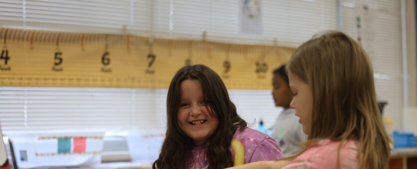 A girl smiles while doing school work at her desk.