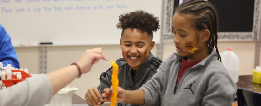 A boy smiles as another boy inspects the consistency of slime he just made