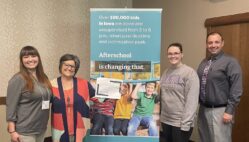 PiECES afterschool program staff and administrators stand on either side of an Iowa Afterschool Alliance banner that reads 