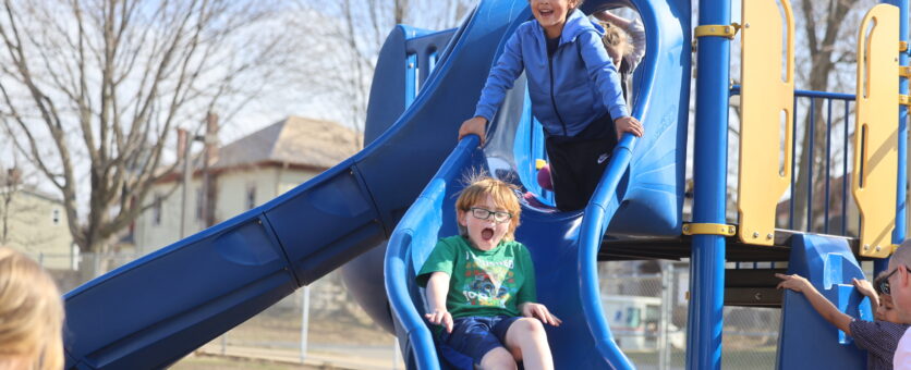 A boy goes down a slide while another boy waits his turn to go after him.