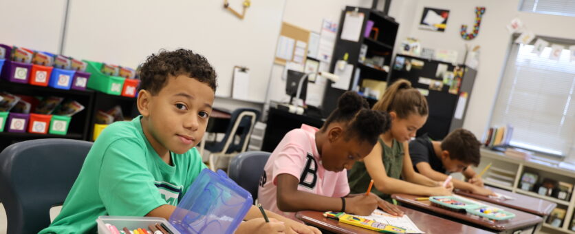 A boy looks up from his work while sitting at his desk in his classroom.