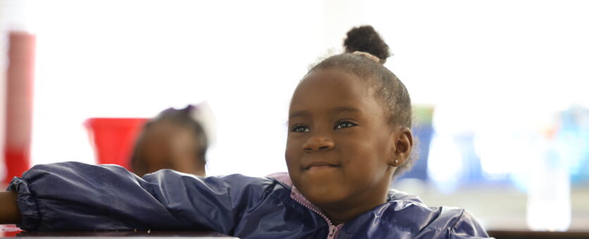 A girl smiles while listening to a book being read by her teacher.