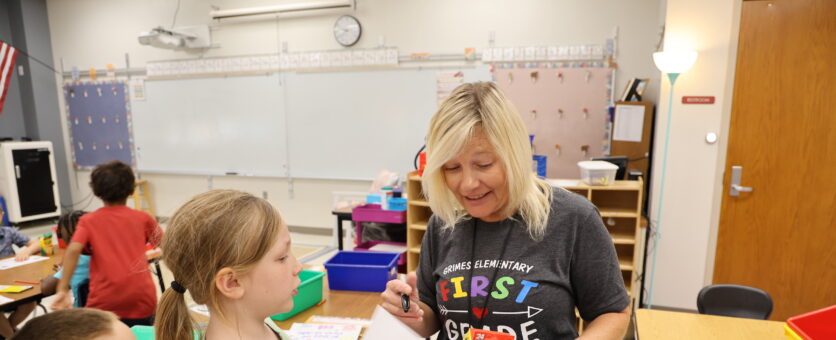 A first grade teacher smiles while talking to an elementary girl