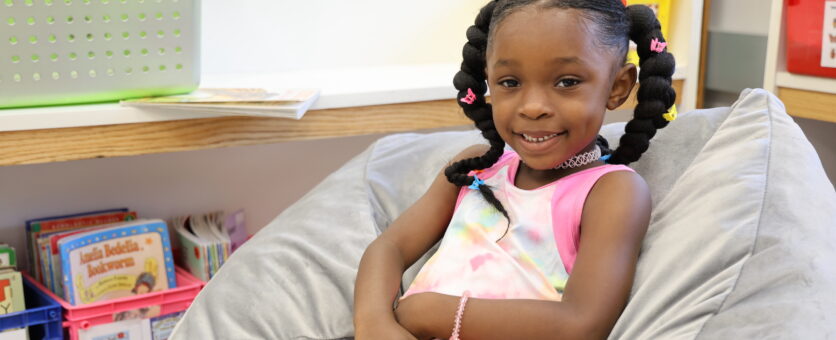 An elementary student smiles while reading a book in a beanbag chair in her classroom