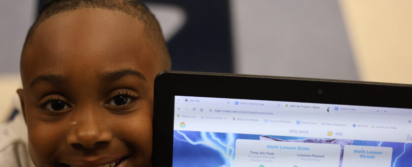 A student smiles while showing off his math progress on his Chromebook screen