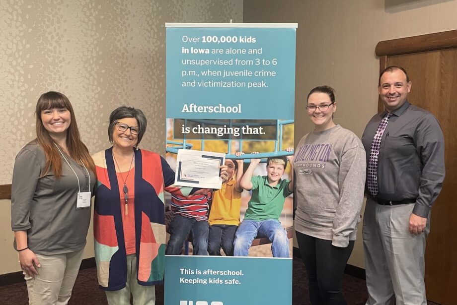 PiECES afterschool program staff and administrators stand on either side of an Iowa Afterschool Alliance banner that reads 