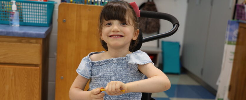 A young girl smiles while coloring in her classroom