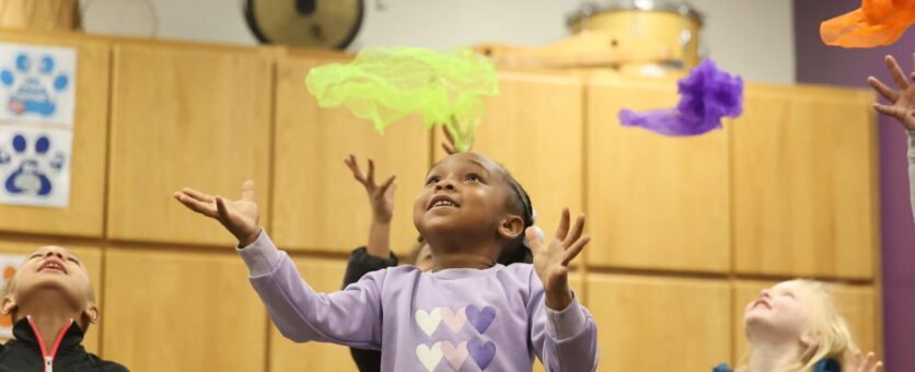 A class of elementary school students throw colorful scarves up in the air during music class