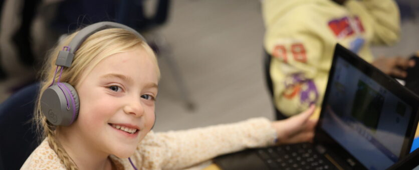 A little girl smiles while for a picture while working on computer coding