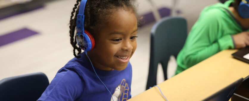 A young boy smiles while learning how to code on his Chromebook.